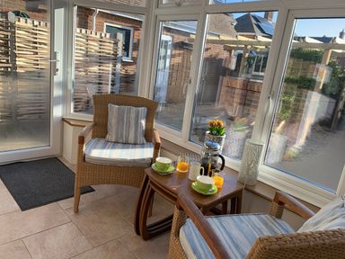 A sunroom with two wicker chairs and a wooden table set with cups glasses teapot and flowers at The Beach House in West Bay