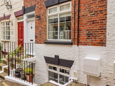 A brick and white painted building exterior with two doors and two windows with plants in pots near stairs at Anchor Cottage in Whitby