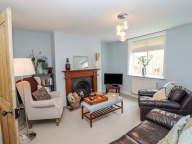 A living room with a fireplace a beige armchair a brown leather sofa a coffee table and a window at Anchor Cottage in Whitby