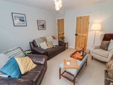 A living room with two leather sofas a fabric armchair coffee table with trays and wine wooden doors and a floor lamp at Anchor Cottage in Whitby