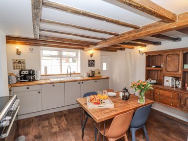 A kitchen with wooden beams on the ceiling a wooden table with chairs and flowers a wooden cabinet and a countertop with appliances at Anchor Cottage in Whitby