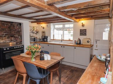 A kitchen with wooden beams on the ceiling a wooden dining table with chairs and flowers a stove and cabinets at Anchor Cottage in Whitby