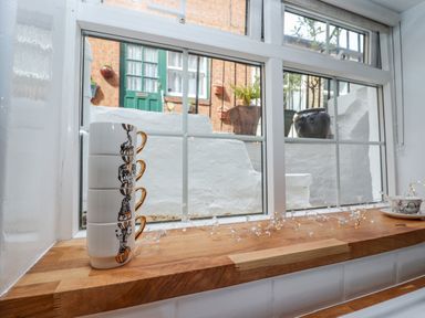 A wooden windowsill with stacked cups and fairy lights looking out to a white wall and green door at Anchor Cottage in Whitby