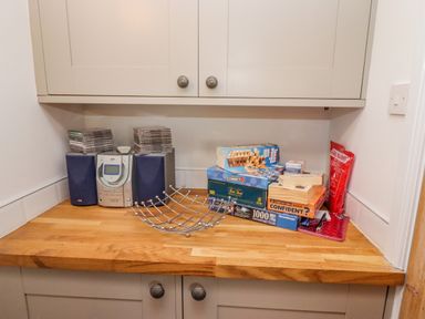 A kitchen counter with a radio stereo system, stacks of CDs, board games, and a metal fruit basket at Anchor Cottage in Whitby