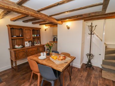 A dining area with a wooden table and chairs a wooden cabinet with mugs and a staircase with a coat rack at Anchor Cottage Whitby
