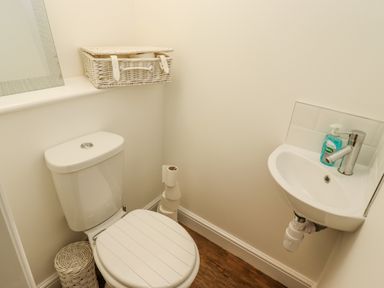 A small bathroom with a toilet a sink a wicker basket a mirror and soap at Anchor Cottage in Whitby