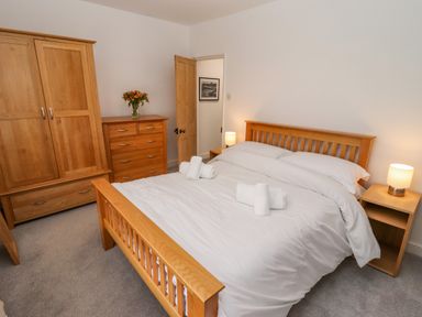A bedroom with a wooden bed frame white bedding two side tables with lamps a wooden wardrobe and dresser with flowers on top at Anchor Cottage Whitby