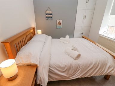 A bedroom with a wooden bed, white bedding, bedside table with lamp and wall decorations at Anchor Cottage in Whitby