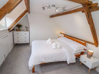 A bedroom with a wooden bedframe white bedding a chest of drawers and bedside table with lamps at Anchor Cottage Whitby
