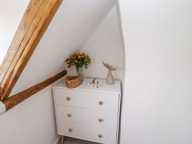 A white chest of drawers with a basket a vase of flowers and a decorative sculpture under a wooden beam at Anchor Cottage in Whitby