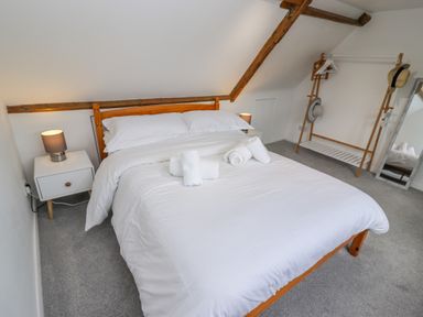 A bedroom with a wooden bed and white bedding two bedside tables with lamps a clothing rack with hats and hangers and a full-length mirror at Anchor Cottage Whitby