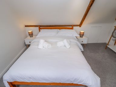 A bedroom with a wooden bed frame white bedding pillows and rolled towels on the bed flanked by two bedside tables with lamps at Anchor Cottage in Whitby