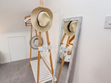 A corner with a wooden coat rack holding hats and hangers next to a full-length mirror at Anchor Cottage in Whitby