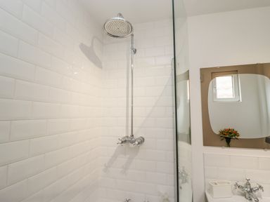 A shower with a rainfall showerhead and a mirror above a sink with a window reflection at Anchor Cottage in Whitby