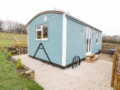 A light blue tiny house on wheels with white trim on a gravel area near a small wooden fence at Robins Nest in Napton-On-The-Hill