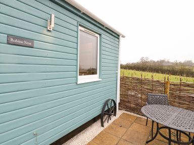 Exterior view of a blue wooden building with a window and metal patio furniture next to a wicker fence at Robins Nest in Napton-On-The-Hill