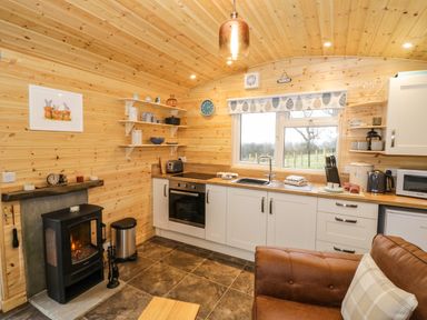A kitchen with white cabinets a stove a sink and a wood stove with a brown leather chair at Robins Nest in Napton-On-The-Hill