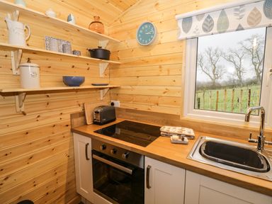 A kitchen with wooden shelves, a stove, a sink, and a window showing trees and a fence at Robins Nest in Napton-On-The-Hill