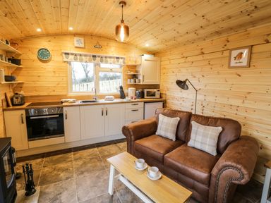 A kitchen and living area with wooden walls a brown sofa a small wooden coffee table and white cabinets at Robins Nest in Napton-On-The-Hill