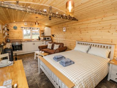 A wooden cabin interior with a bed sofa kitchen and dining table at Robins Nest in Napton-On-The-Hill