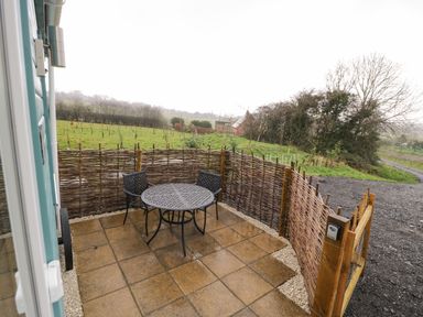 A small outdoor patio with a round metal table and two chairs enclosed by a woven wooden fence at Robins Nest in Napton-On-The-Hill