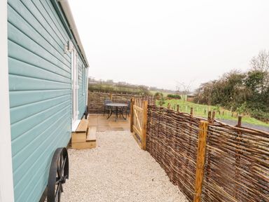 Side area of a blue cabin with wooden steps gravel pathway wicker fence and a round metal table with chairs at Robins Nest in Napton-On-The-Hill