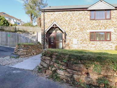 The exterior of a stone cottage with a paved walkway and stone retaining walls at Brewers Cottage in Looe