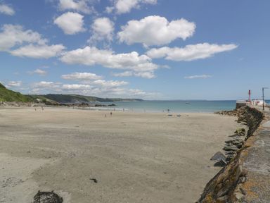 A sandy beach with people near the water and a stone pier with a red light at Brewers Cottage in Looe