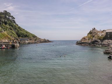 A coastal inlet with clear water surrounded by rocky cliffs and greenery at Brewers Cottage in Looe