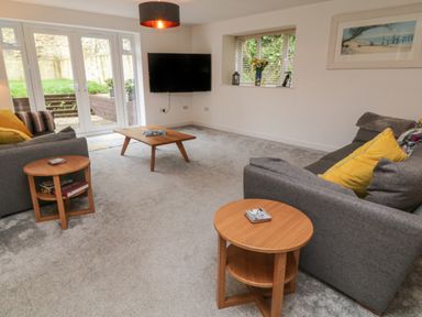 A living room with two gray sofas yellow cushions wooden coffee tables wall-mounted TV and large glass doors at Brewers Cottage in Looe