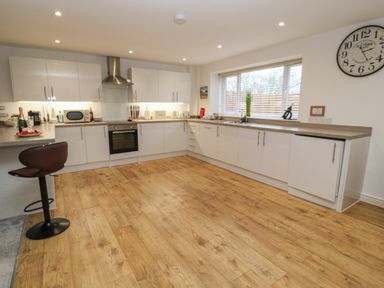 A kitchen with white cabinets wooden floor a bar stool and a large window at Brewers Cottage in Looe