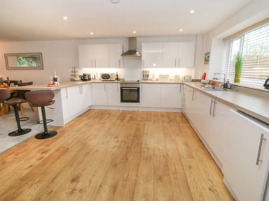 A kitchen with white cabinets wooden floor a stove microwave sink and bar stools at Brewers Cottage in Looe