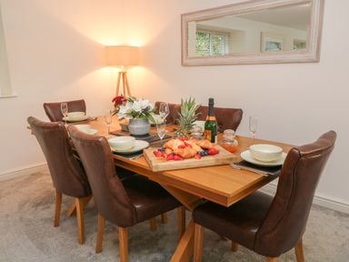 A dining room with a wooden table set with croissants fruit and a bottle with six brown chairs Brewers Cottage Looe
