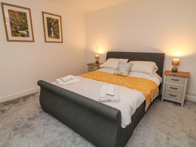 A bedroom with a bed with yellow throw and two bedside tables with lamps at Brewers Cottage in Looe