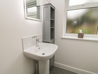 A bathroom sink with a faucet a grey shelving unit a window with a tissue box on the sill and a mirror on the wall at Brewers Cottage in Looe