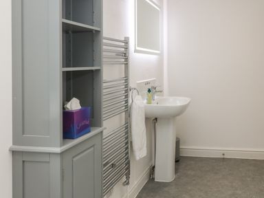 A bathroom with a pedestal sink towel holder mirror towel rack and shelving unit at Brewers Cottage in Looe