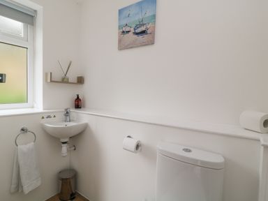 A bathroom with a toilet sink towel holder trash can and a painting at Brewers Cottage in Looe