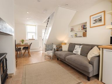 A living room with a gray sofa a small armchair a dining table with chairs and a staircase at Quayside Cottage in Teignmouth
