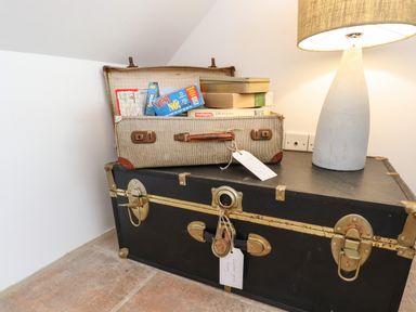 An open vintage suitcase with board games on top of a black trunk next to a lamp in a corner of a room at Quayside Cottage in Teignmouth
