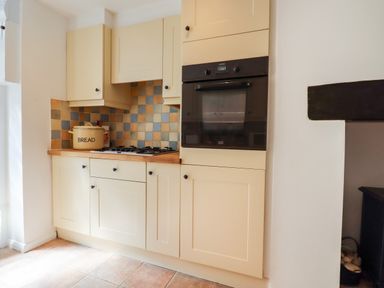 A kitchen with cream cabinetry a built in oven a gas stove and a bread container on the countertop at Quayside Cottage in Teignmouth