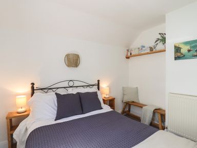 A bedroom with a bed a wooden bench a bookshelf and two bedside lamps at Quayside Cottage in Teignmouth