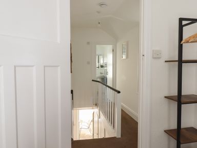 A hallway with a staircase leading down and a bathroom at the end of the hall at Quayside Cottage in Teignmouth