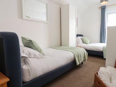 A bedroom with two single beds with green pillows and blankets a white wardrobe and a window with blue curtains at Quayside Cottage in Teignmouth