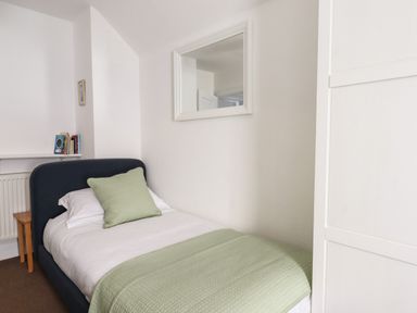 A small bedroom with a single bed green pillow and green blanket a small wooden table and books on a shelf at Quayside Cottage in Teignmouth