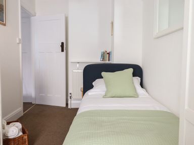A small bedroom with a single bed a green pillow and blanket and a basket with towels at Quayside Cottage in Teignmouth
