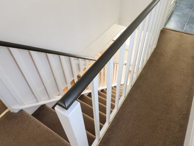 A carpeted staircase with white railings and black handrails leading down to a lower floor in a hallway at Quayside Cottage in Teignmouth