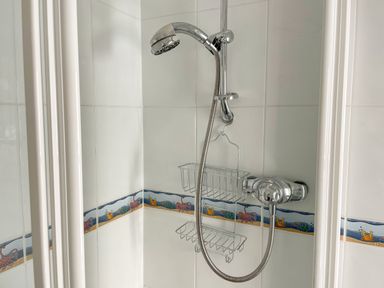 A showerhead with a hose and two metal baskets attached to tiled walls with a nautical border at Quayside Cottage in Teignmouth