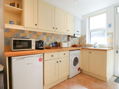 A kitchen with cream cabinets a microwave washing machine refrigerator and a window at Quayside Cottage in Teignmouth