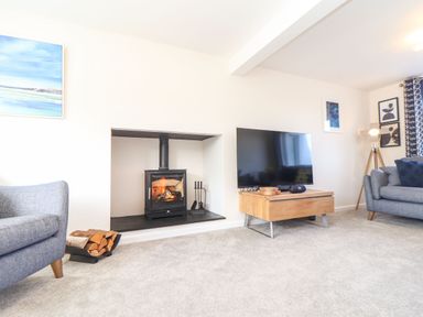 A living room with a wood burning stove television and grey sofas at Pickney House in Killigarth near Polperro