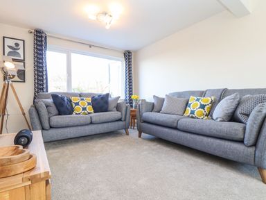 A living room with two grey sofas and patterned cushions at Pickney House Killigarth near Polperro